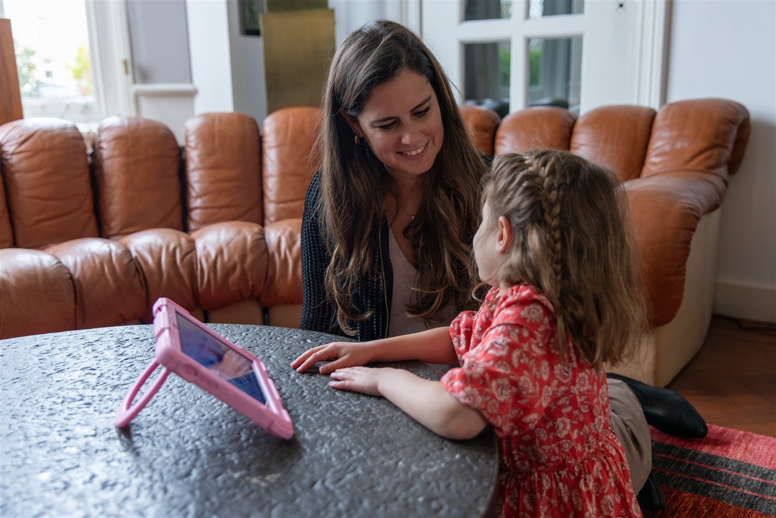Lisanne en een kind aan tafel kijken elkaar aan, de roze kinder-iPad ligt ernaast