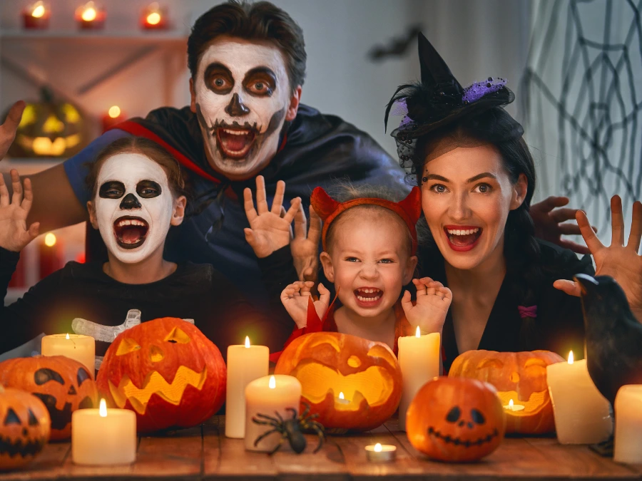 Gezin in Halloweenkostuums met geschminkte gezichten achter een tafel vol pompoenen en kaarsen